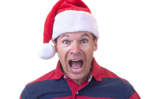 Stressed out Caucasian man wearing red Santa hat screams in disbelief on white background