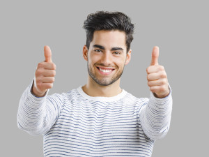 Portrait of handsome young man with thumbs up, isolated over a gray background