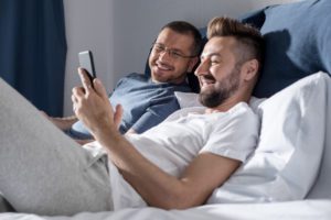 gay couple in bed with iphone istock photo