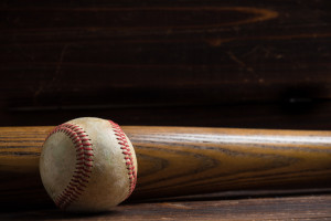 Baseball equipment: wooden bat and ball on a wood plank or bench background