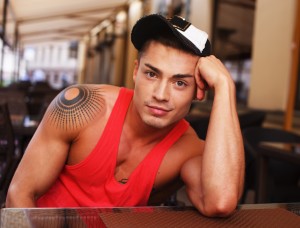 Stylish young man in cap sitting behind table in summer cafe