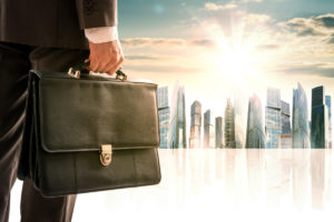 Businessman with suitcase against morning modern city, rear view