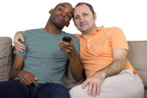 interracial gay male couple on couch with remote deposit photo 9 24 21