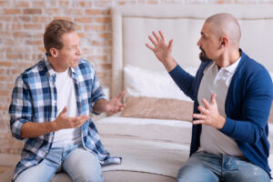 gay male couple arguing on a bed one white one latino blue shirts