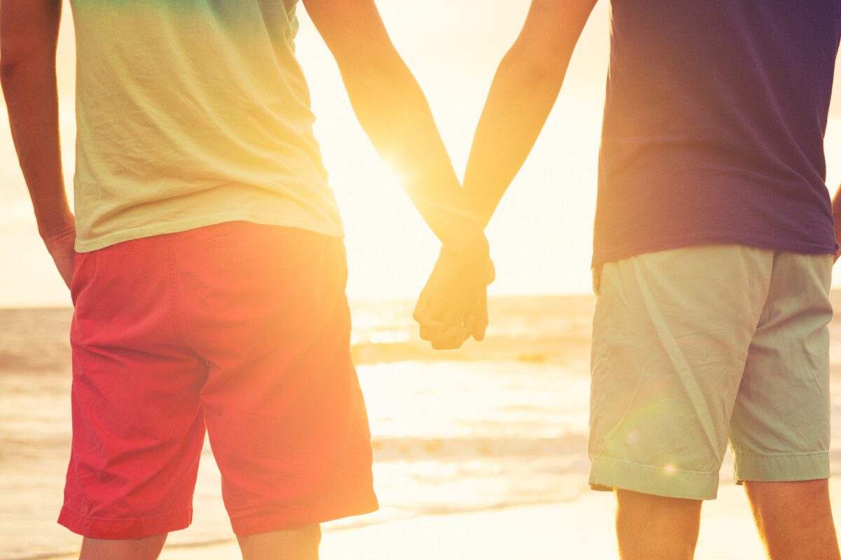 gay couple holding hands at beach at sunset deposit photo June 2022 podcast
