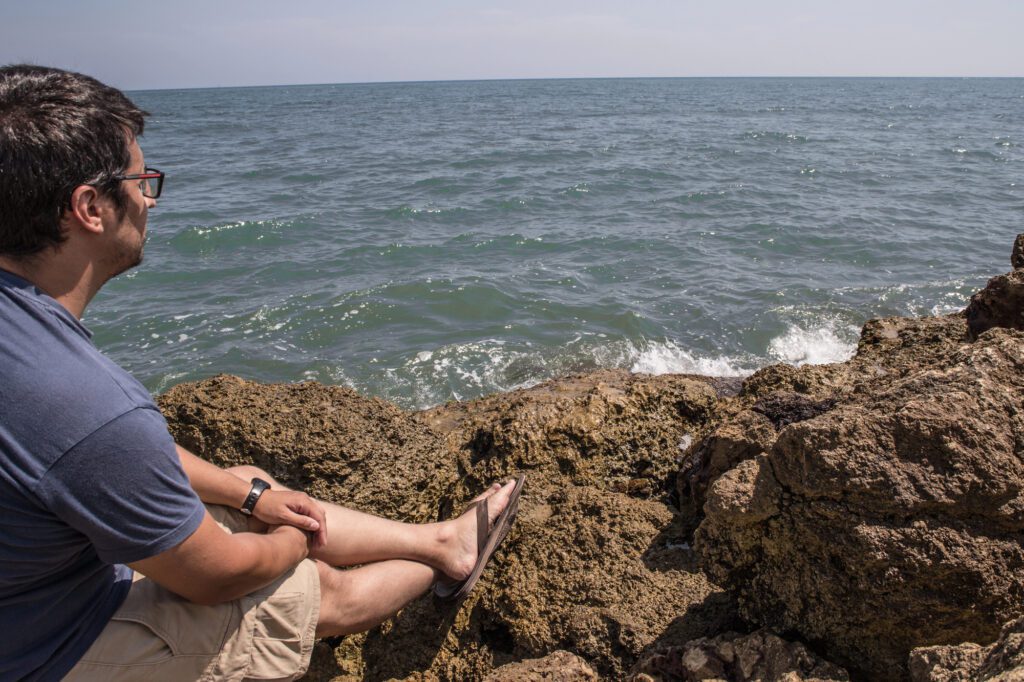 Man looking at the sea on the stones of the shore