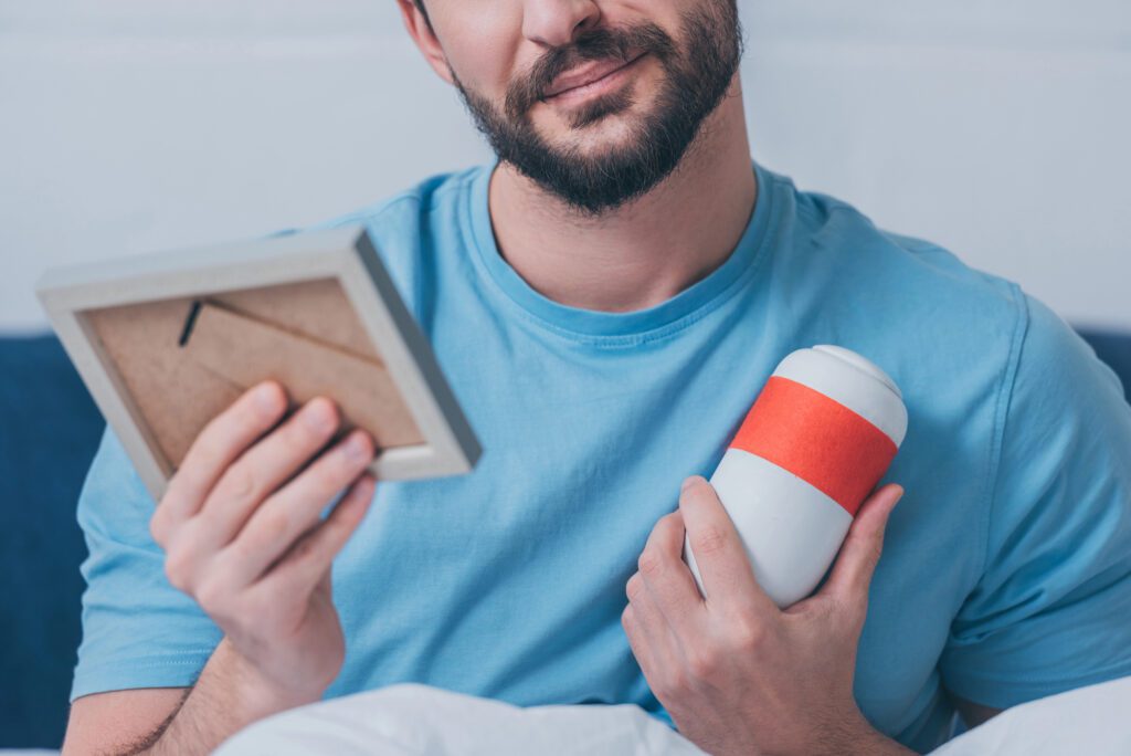 man holding photo frame and funeral urn at home