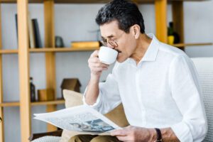 Senior man in glasses drinking coffee and reading newspaper at home