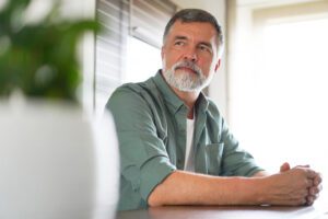 s Happy attractive mature man sitting at table in kitchen.