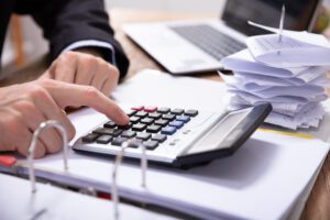 Close-up Of Businessman's Hand Using Calculator While Calculating Invoice On Desk