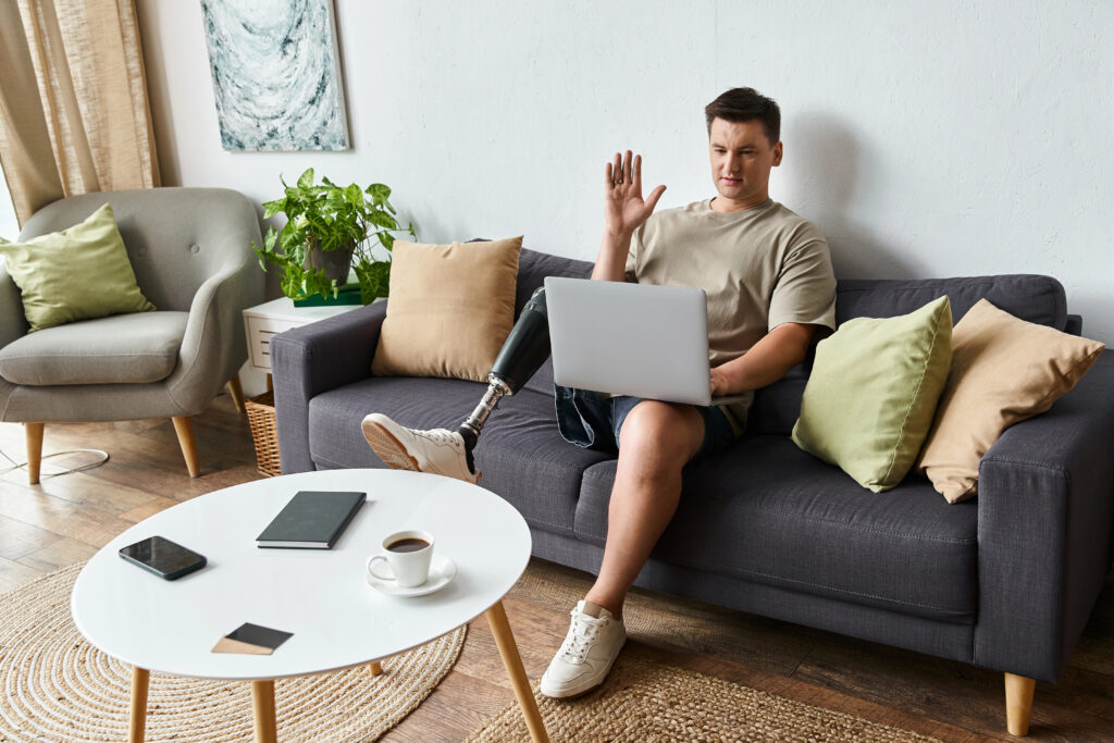 Handsome young man with prosthetic leg engages in video call from comfortable couch at home.