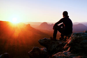 Mature man existing confidently alone, looking into the sunset on top of a mountain