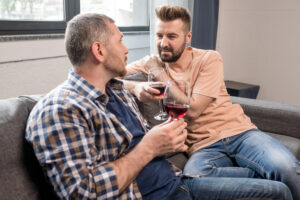 Two men in a relationship talking together over glasses of wine at home.