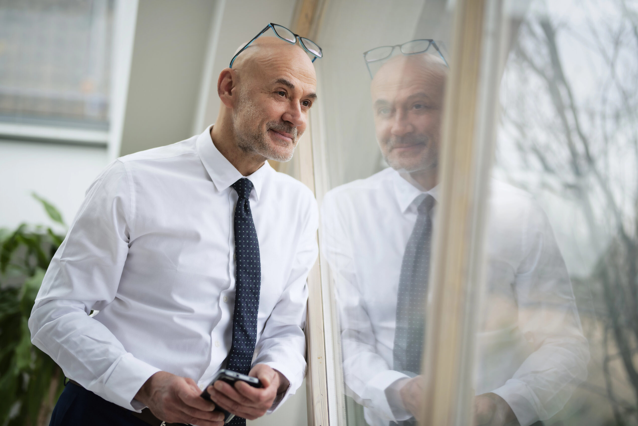 Smiling gay businessman wearing shirt and tie and looking thougthfully while standing at the window.