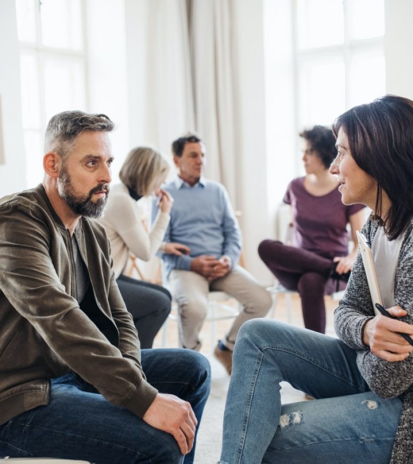 senior counselor with clipboard talking to a man during group therapy senior counselor with clipboard talking to a man during group therapy